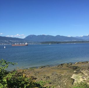 A view of the water of Burrard Inlet from the beach, there is a ship in the distance.