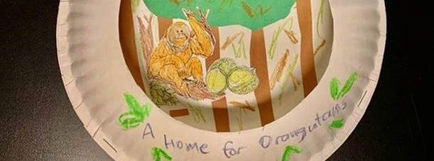 Two paper plates have been fashioned into a window shape. Inside the cut out is an orangutan in a forest. On the outside, "A Home for Orangutans" is written.